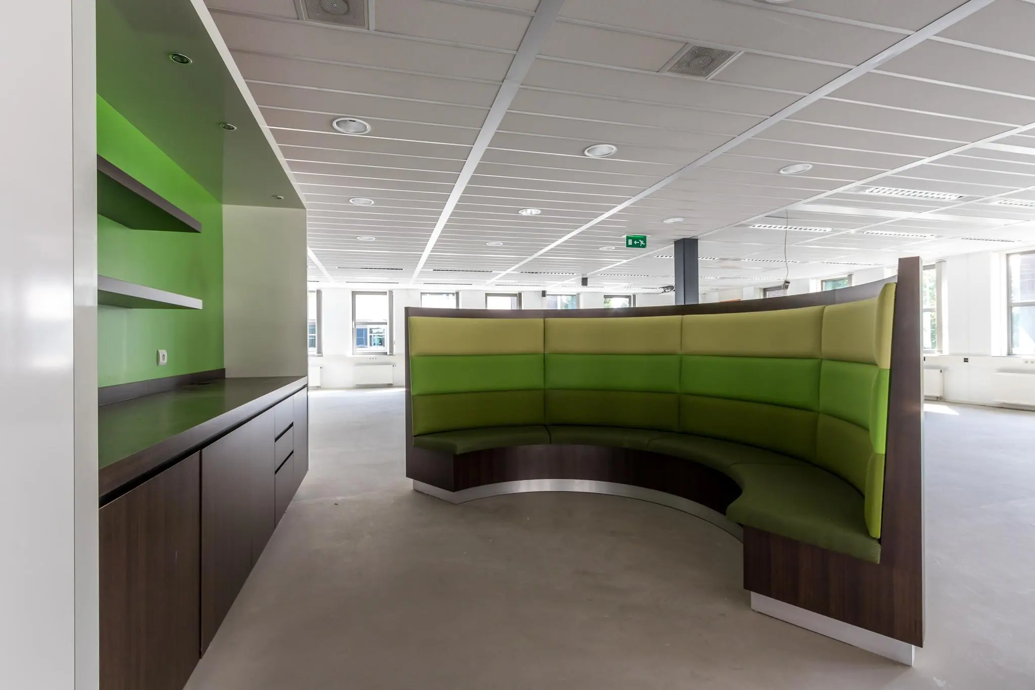 Moderne kantoorruimte met een ronde groene zithoek en een wandmeubel met open planken.